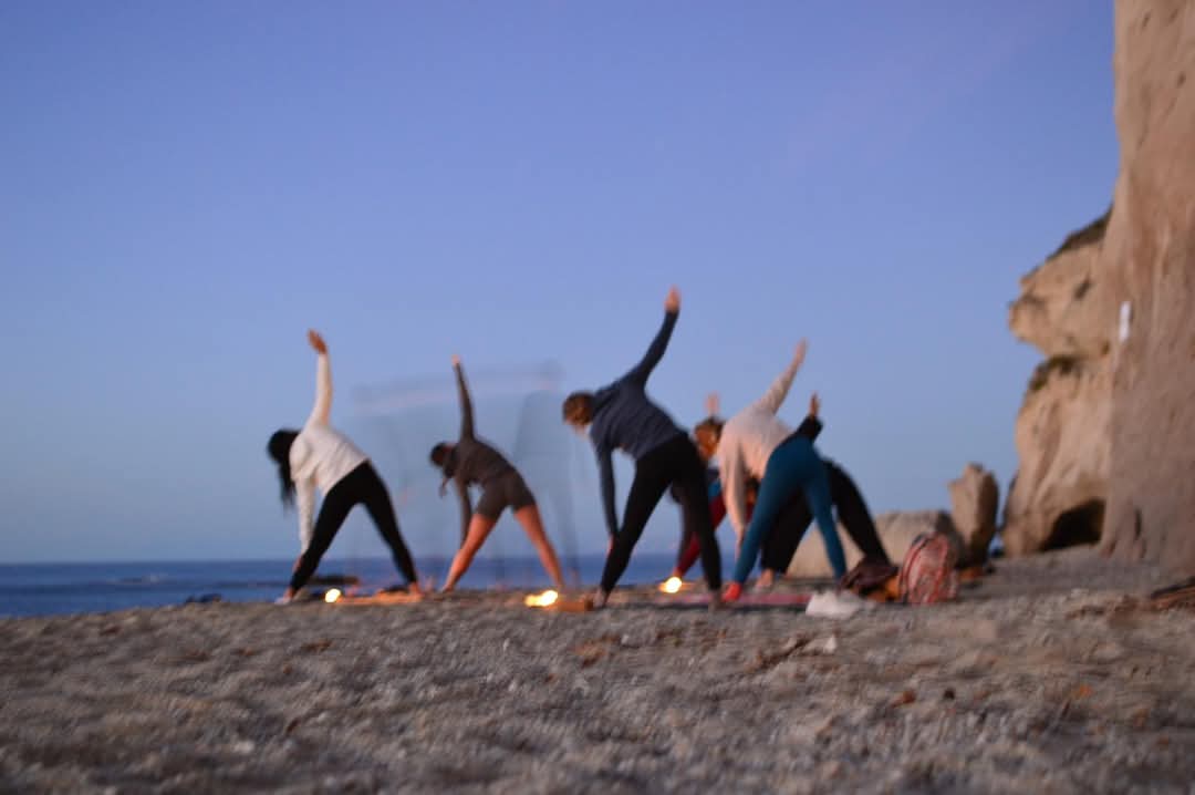 group doing yoga standing by the sea